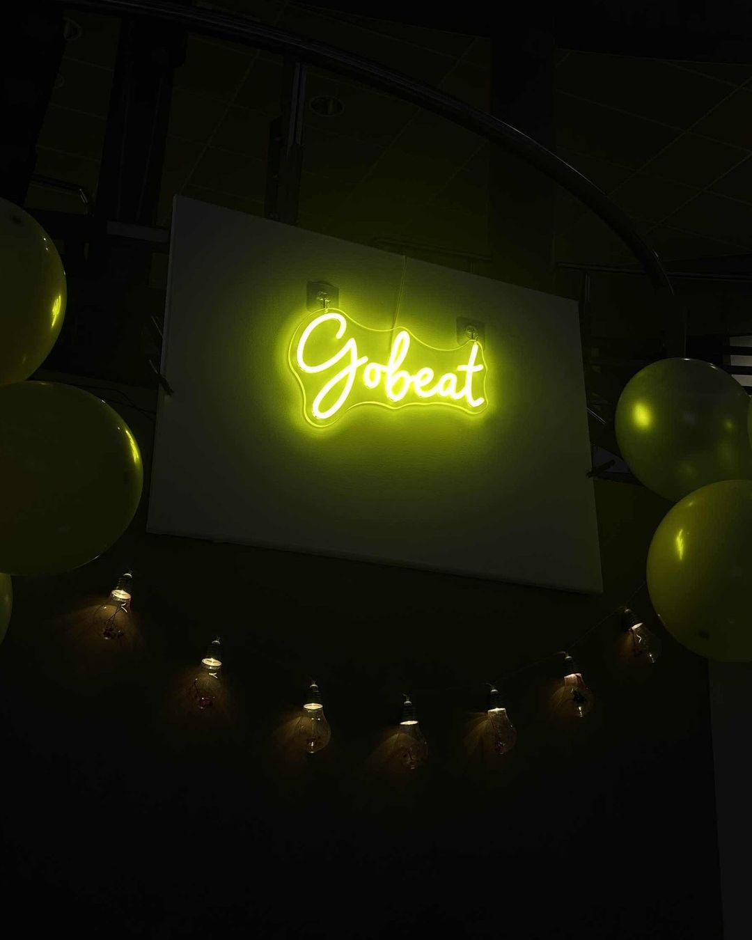Enseigne au néon jaune « Gobeat » au-dessus du stand, entre des ballons et une guirlande d'ampoules.